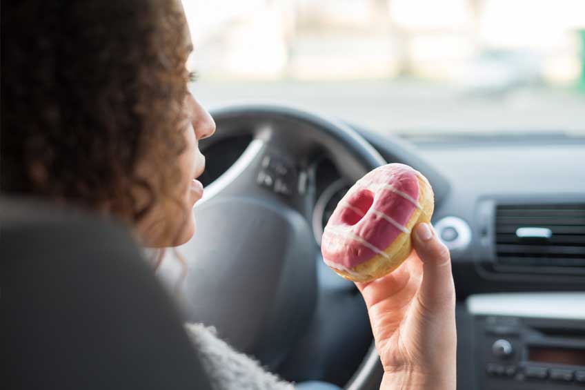 woman in car eating a frosted donut