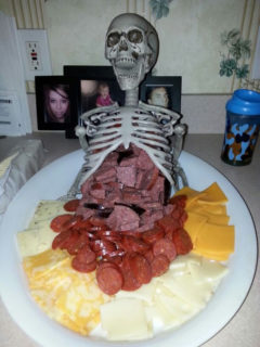 Very disturbing halloween sausage and cheese presentation featuring a skeleton with sausage and cheese coming out of his innards 